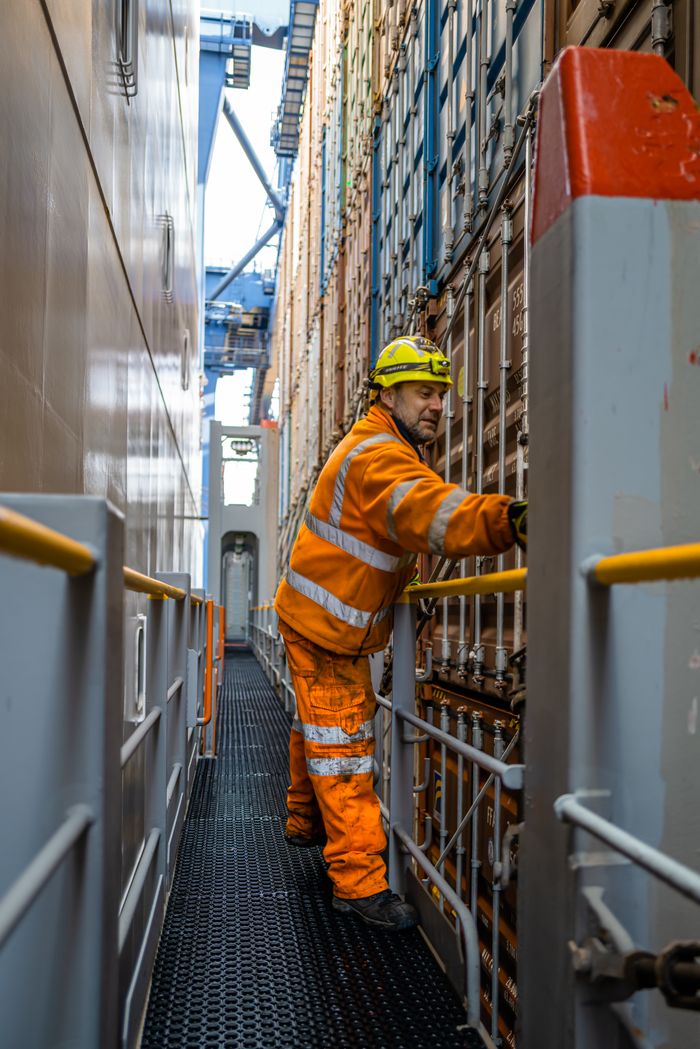 A worker in safety gear manages cargo containers on a ship in Felixstowe port.